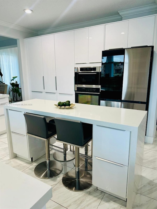 kitchen with crown molding, a kitchen bar, light countertops, stainless steel double oven, and white cabinets