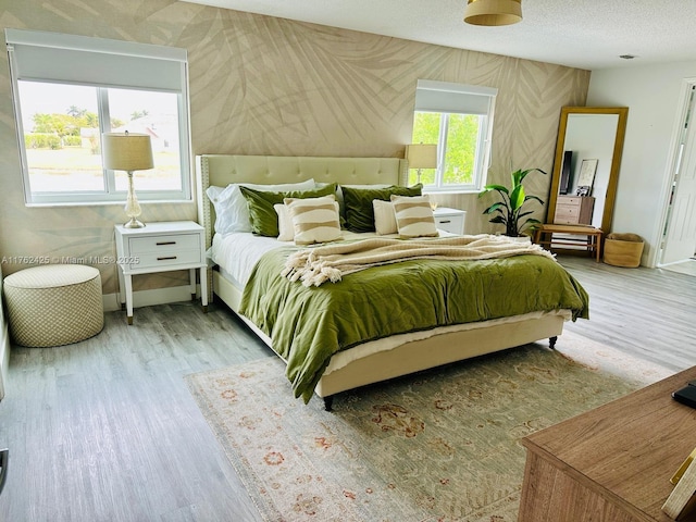 bedroom featuring a textured ceiling, wallpapered walls, baseboards, and wood finished floors