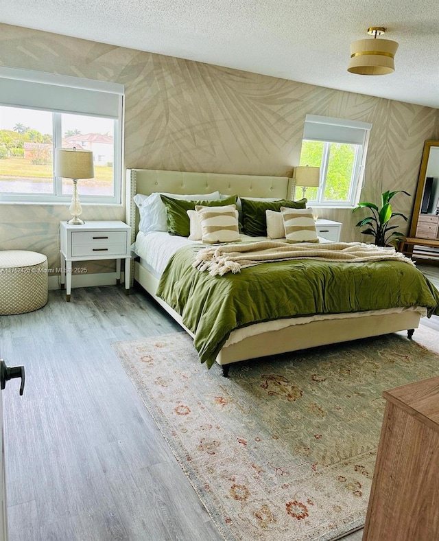 bedroom featuring a textured ceiling, wallpapered walls, and wood finished floors