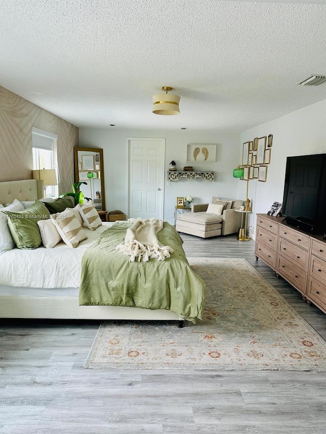 bedroom with wood finished floors, visible vents, and a textured ceiling