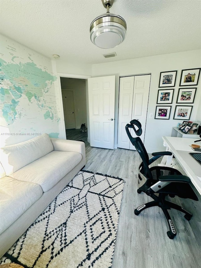 office space with visible vents, light wood-style floors, and a textured ceiling