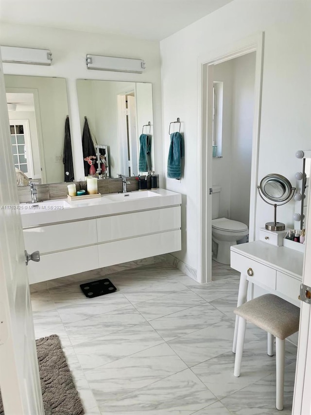 bathroom featuring a sink, toilet, marble finish floor, and double vanity