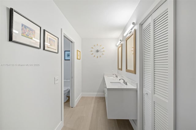 bathroom with baseboards, toilet, double vanity, wood finished floors, and a closet