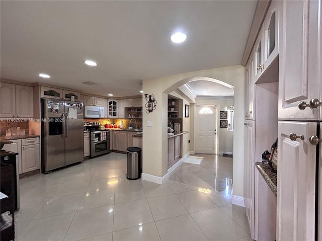 kitchen featuring glass insert cabinets, light tile patterned flooring, arched walkways, stainless steel appliances, and a sink