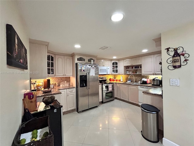 kitchen with tasteful backsplash, glass insert cabinets, light tile patterned floors, stainless steel appliances, and a sink