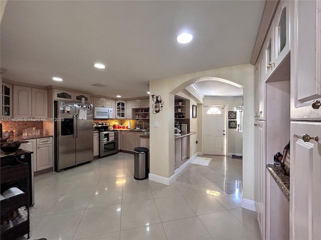 kitchen featuring a sink, arched walkways, appliances with stainless steel finishes, light tile patterned flooring, and glass insert cabinets