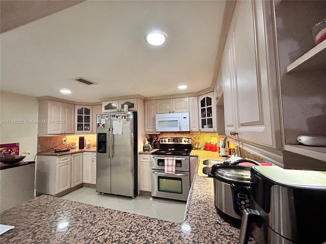 kitchen with decorative backsplash, glass insert cabinets, visible vents, and stainless steel appliances