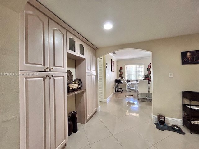 hallway with arched walkways, crown molding, baseboards, and light tile patterned flooring