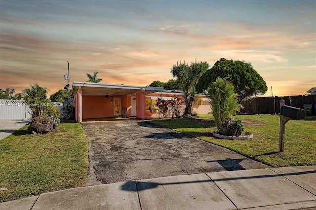 view of front facade featuring fence, concrete driveway, a yard, a carport, and a ceiling fan