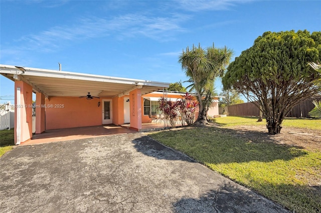 ranch-style home featuring a ceiling fan, driveway, stucco siding, a carport, and a front lawn