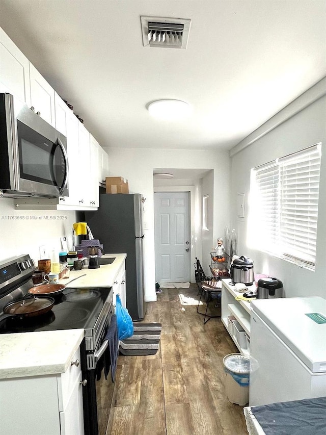929 SW 12th Ave, Miami, FL 33130 - kitchen with visible vents, wood finished floors, white cabinetry, stainless steel appliances, and light countertops