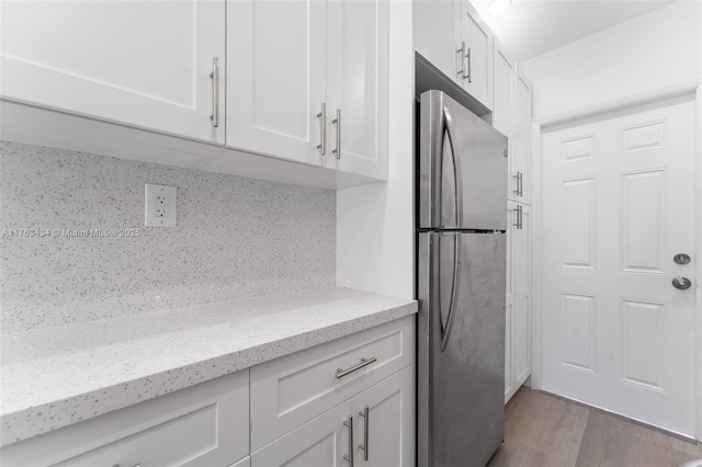 kitchen with tasteful backsplash, light stone counters, freestanding refrigerator, light wood-style floors, and white cabinets