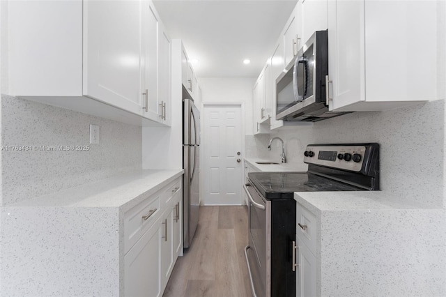 kitchen with light wood-style flooring, a sink, decorative backsplash, appliances with stainless steel finishes, and white cabinetry