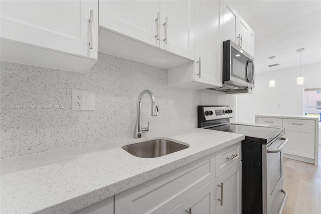 kitchen with tasteful backsplash, light stone countertops, stainless steel appliances, white cabinetry, and a sink