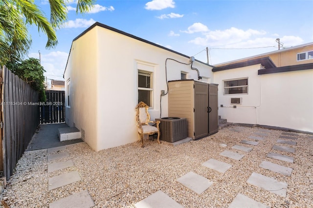 rear view of house with stucco siding, central AC unit, an outdoor structure, and fence