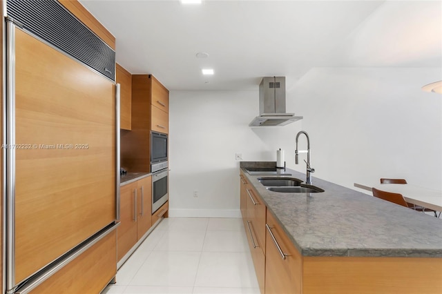kitchen featuring light tile patterned floors, island exhaust hood, brown cabinetry, paneled refrigerator, and a sink