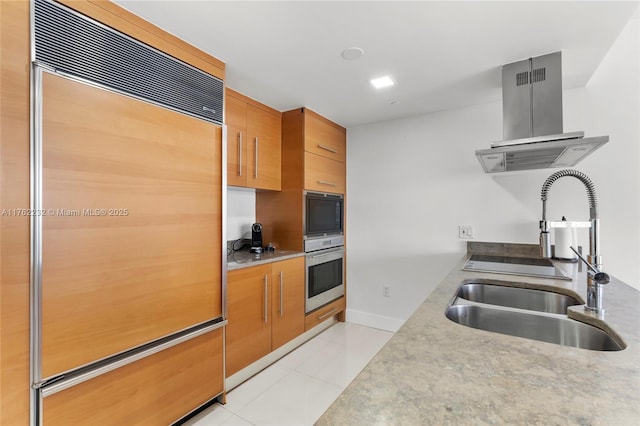 kitchen featuring a sink, brown cabinetry, island range hood, light tile patterned floors, and built in appliances