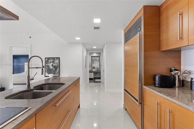 kitchen with visible vents, a sink, light stone counters, light tile patterned floors, and built in fridge