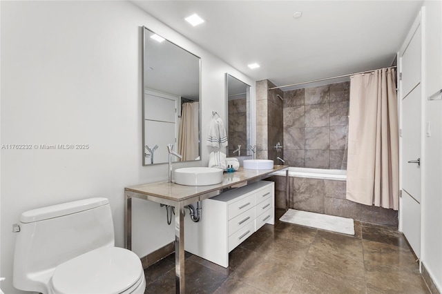 bathroom featuring double vanity, a sink, stone finish flooring, toilet, and tiled shower / bath
