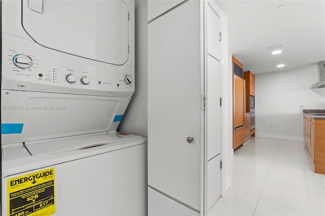 laundry area with laundry area, stacked washer and dryer, light tile patterned floors, and baseboards