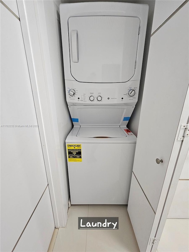 clothes washing area featuring laundry area, stacked washer and dryer, and light tile patterned floors