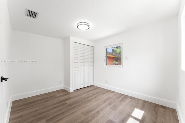 unfurnished bedroom featuring wood finished floors, visible vents, a closet, and baseboards