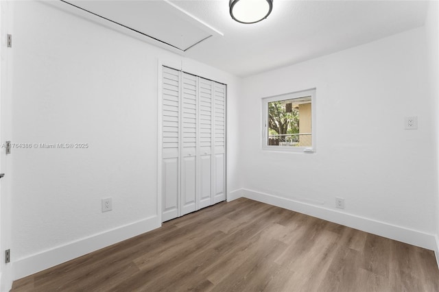 unfurnished bedroom with a closet, baseboards, attic access, and wood finished floors