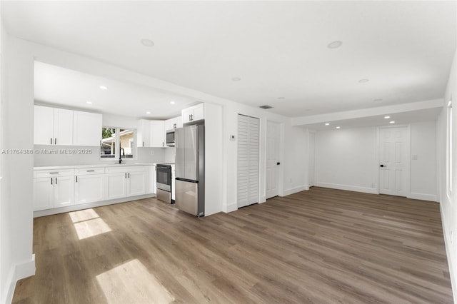 kitchen with light wood finished floors, open floor plan, white cabinetry, stainless steel appliances, and light countertops