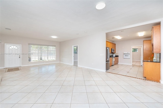 unfurnished living room featuring light tile patterned floors, visible vents, a healthy amount of sunlight, and baseboards