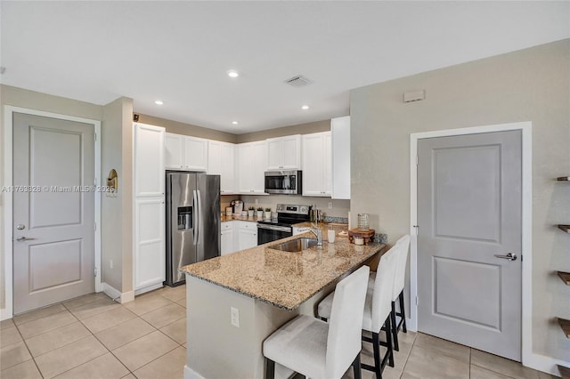 kitchen with a breakfast bar area, light stone counters, a peninsula, stainless steel appliances, and white cabinetry