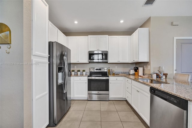 kitchen featuring visible vents, light stone countertops, white cabinets, stainless steel appliances, and a sink