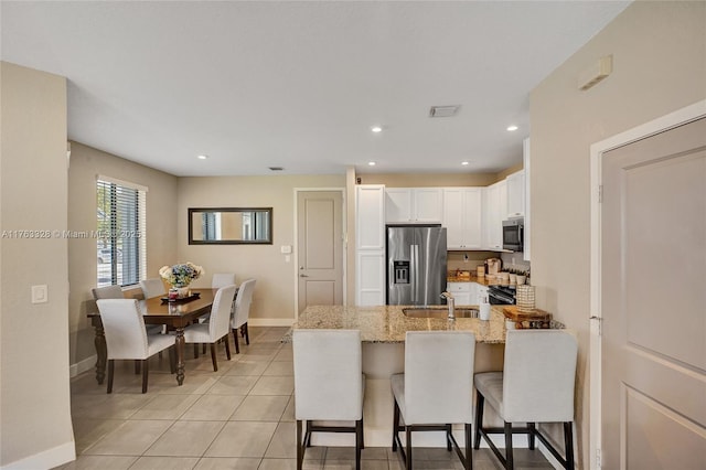 kitchen with light stone countertops, appliances with stainless steel finishes, a peninsula, white cabinets, and a sink