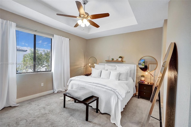 bedroom with carpet flooring, baseboards, a tray ceiling, and a ceiling fan