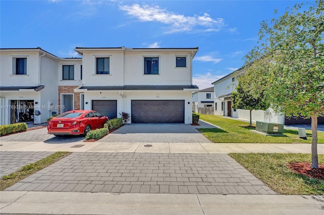 view of front of home featuring a front yard, fence, an attached garage, stucco siding, and decorative driveway