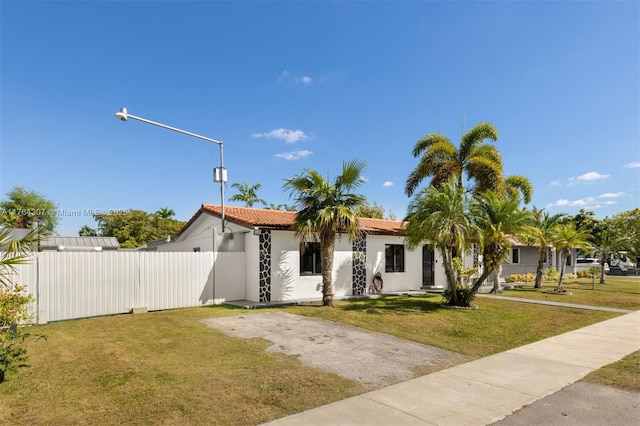 view of front of home with a tiled roof, stucco siding, a front yard, and fence