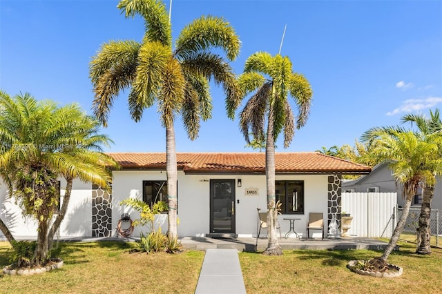 view of front of house with stucco siding, a tile roof, a front yard, and fence