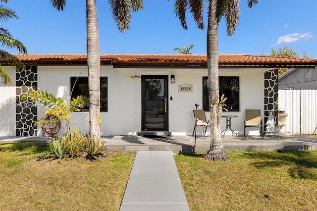 view of front of house with a front lawn, a tiled roof, fence, and stucco siding