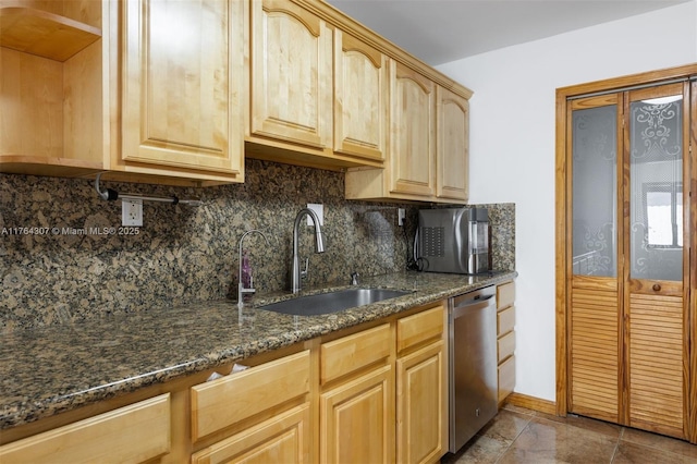 kitchen featuring light brown cabinetry, a sink, tasteful backsplash, stainless steel dishwasher, and dark stone counters