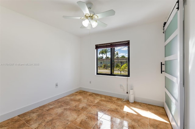 unfurnished room with a barn door, baseboards, and ceiling fan