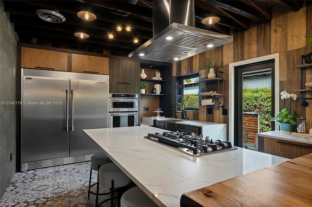 kitchen featuring wooden walls, open shelves, a sink, appliances with stainless steel finishes, and exhaust hood