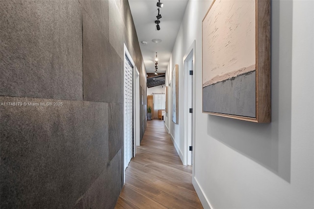 hall with rail lighting, wood finished floors, and baseboards