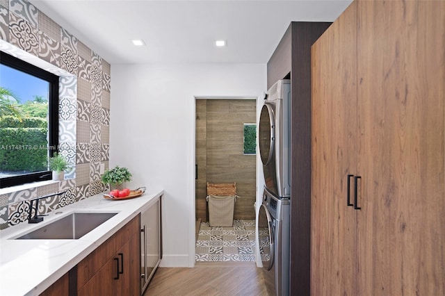 kitchen featuring a sink, light stone counters, refrigerator, light wood-style floors, and stacked washer / drying machine