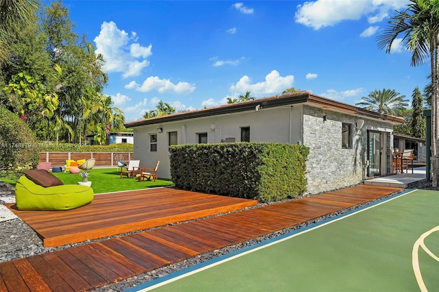 rear view of property with stone siding, stucco siding, a deck, and fence