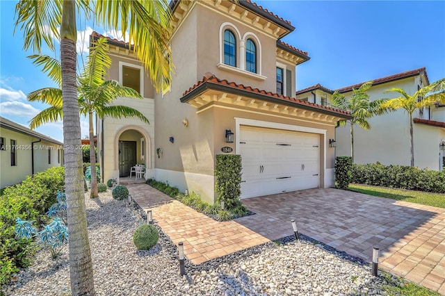 mediterranean / spanish house featuring stucco siding, an attached garage, a tile roof, and decorative driveway