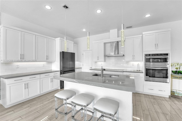 kitchen featuring wood tiled floor, stainless steel double oven, a sink, decorative backsplash, and white cabinetry