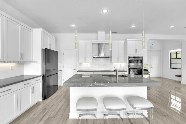 kitchen featuring a breakfast bar, a sink, freestanding refrigerator, double oven, and wall chimney exhaust hood