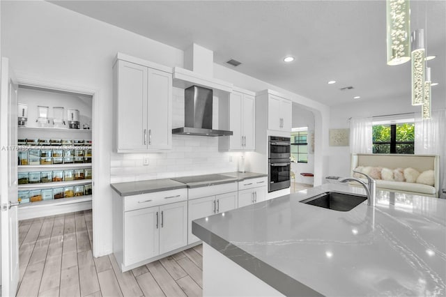 kitchen featuring black electric stovetop, double oven, decorative backsplash, wall chimney exhaust hood, and a sink