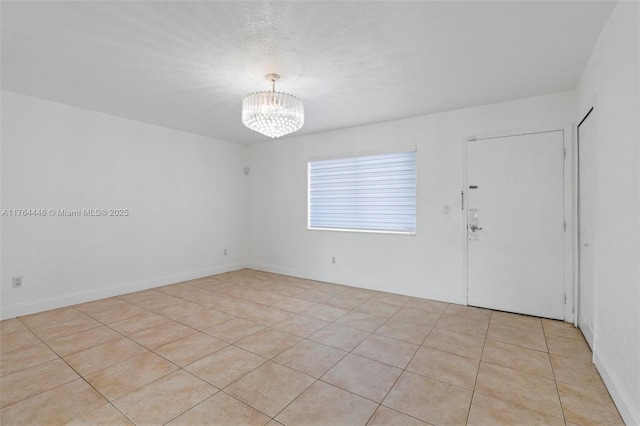 empty room featuring a notable chandelier, a textured ceiling, and baseboards