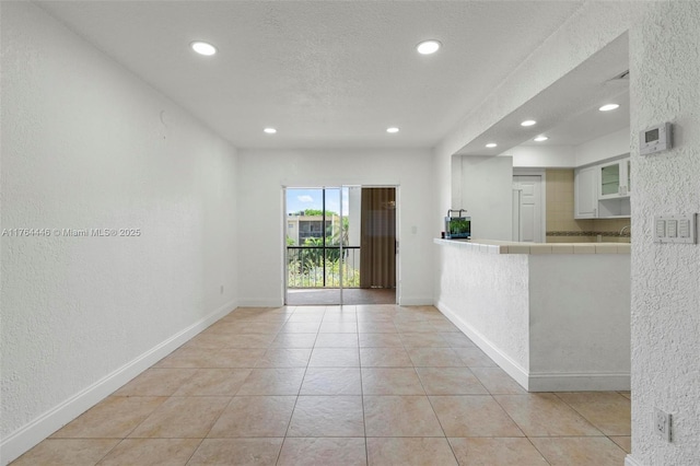 empty room with light tile patterned flooring, recessed lighting, baseboards, and a textured wall