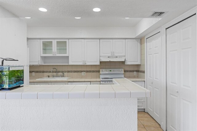 kitchen with under cabinet range hood, tile countertops, white electric stove, and a sink